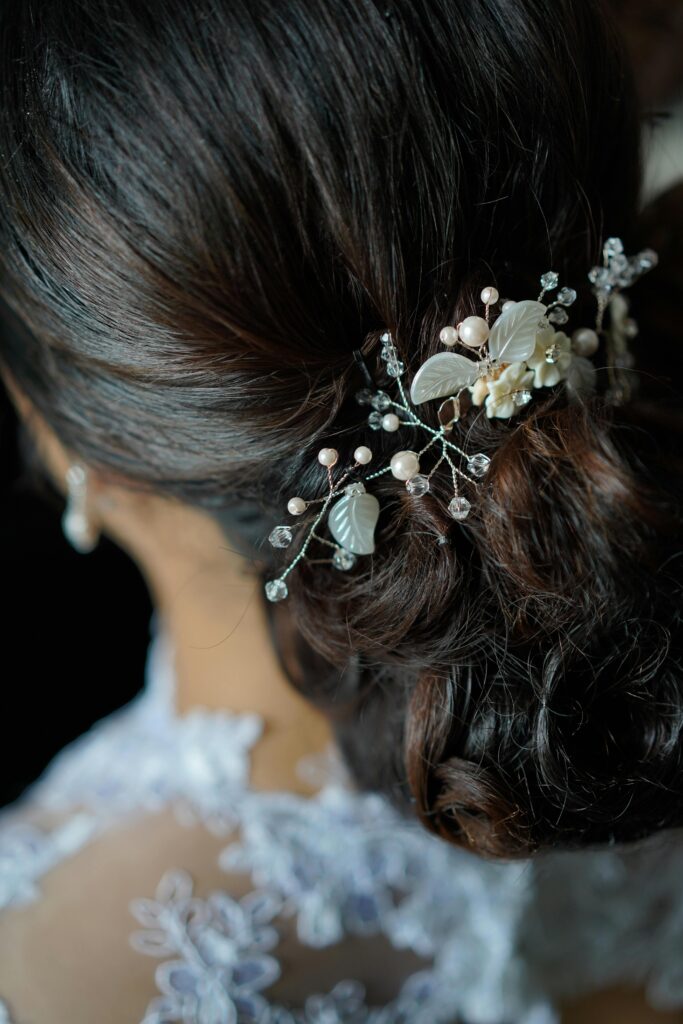 Detalle de peinado semirecogido para novia con cabello oscuro, decorado con un tocado de flores y perlas en un entorno natural. Detalle de peinado semirecogido para novia con cabello oscuro, decorado con un tocado de flores y perlas en un entorno natural.