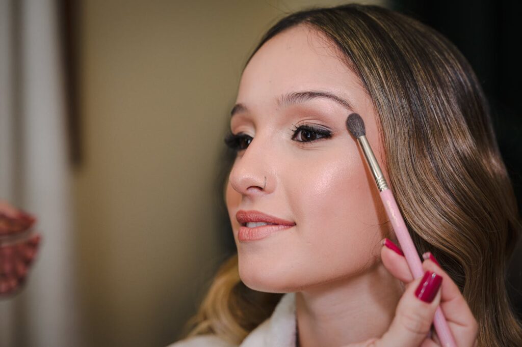 Primer plano de una joven aplicándose maquillaje con una brocha, mostrando belleza y elegancia.
