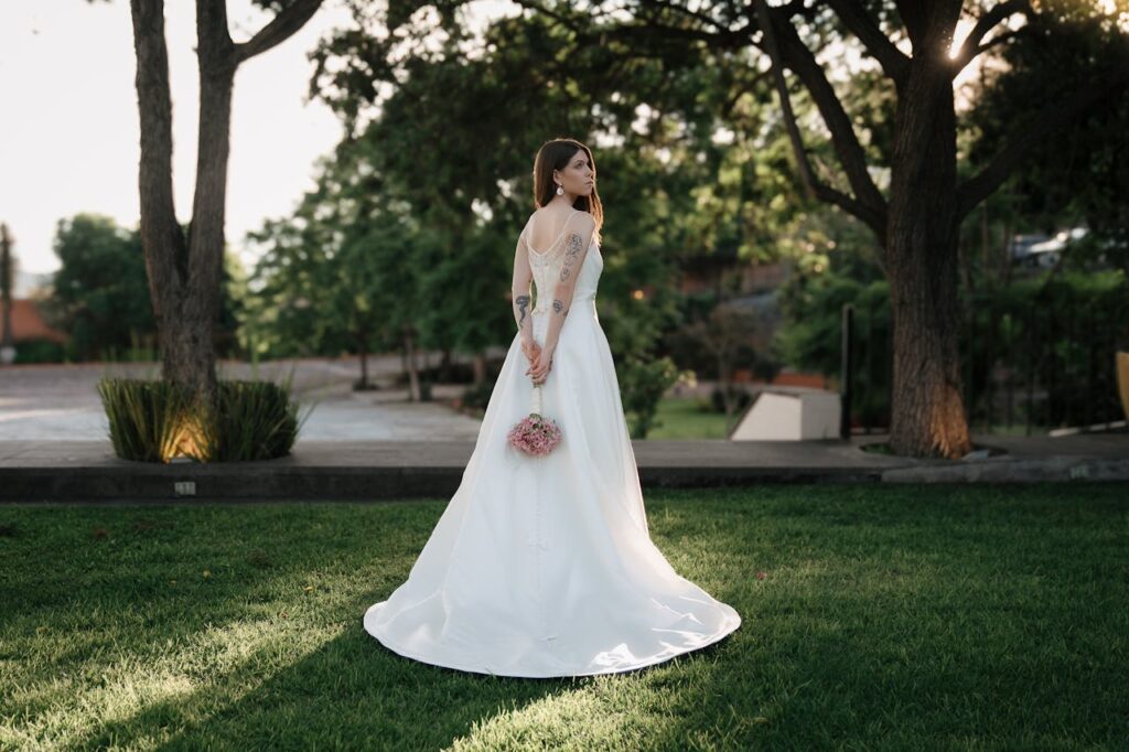 Novia sola de espaldas en un jardín con pelo liso y vestido de novia blanco, representando un servicio de maquillaje profesional personalizado para bodas en Barcelona.