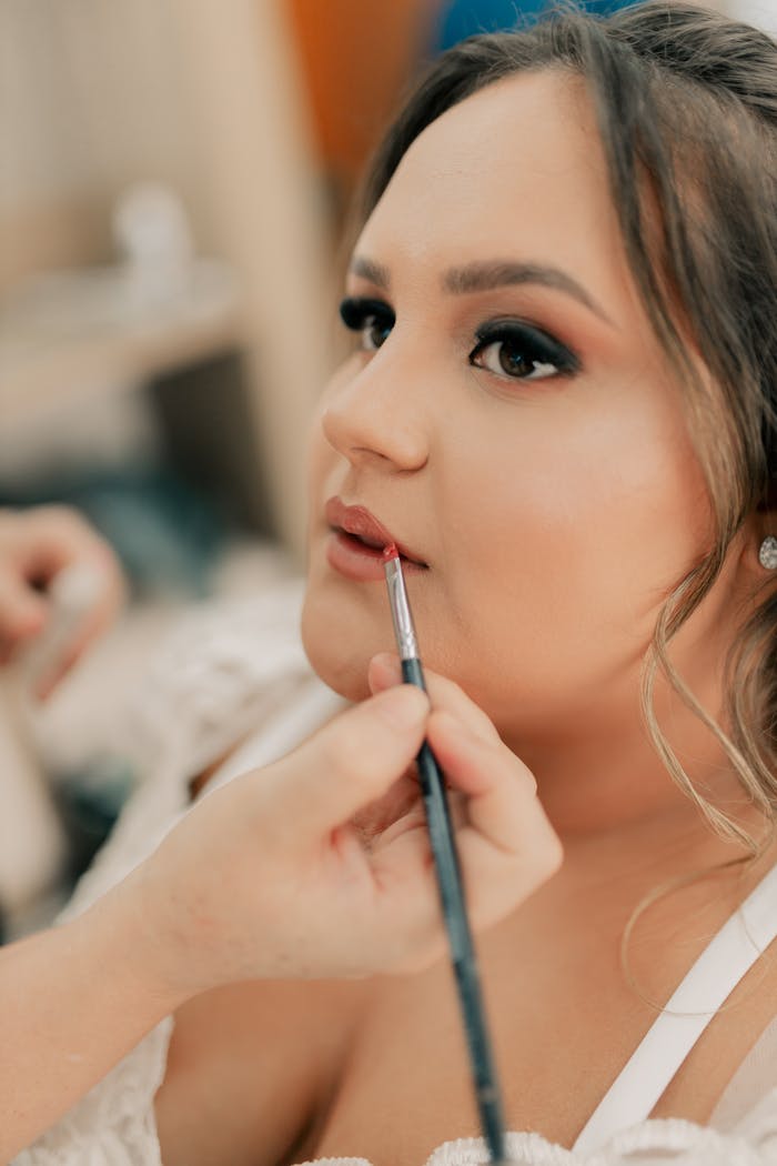 A makeup artist skillfully applies lipstick to a bride's lips, focusing on detail.