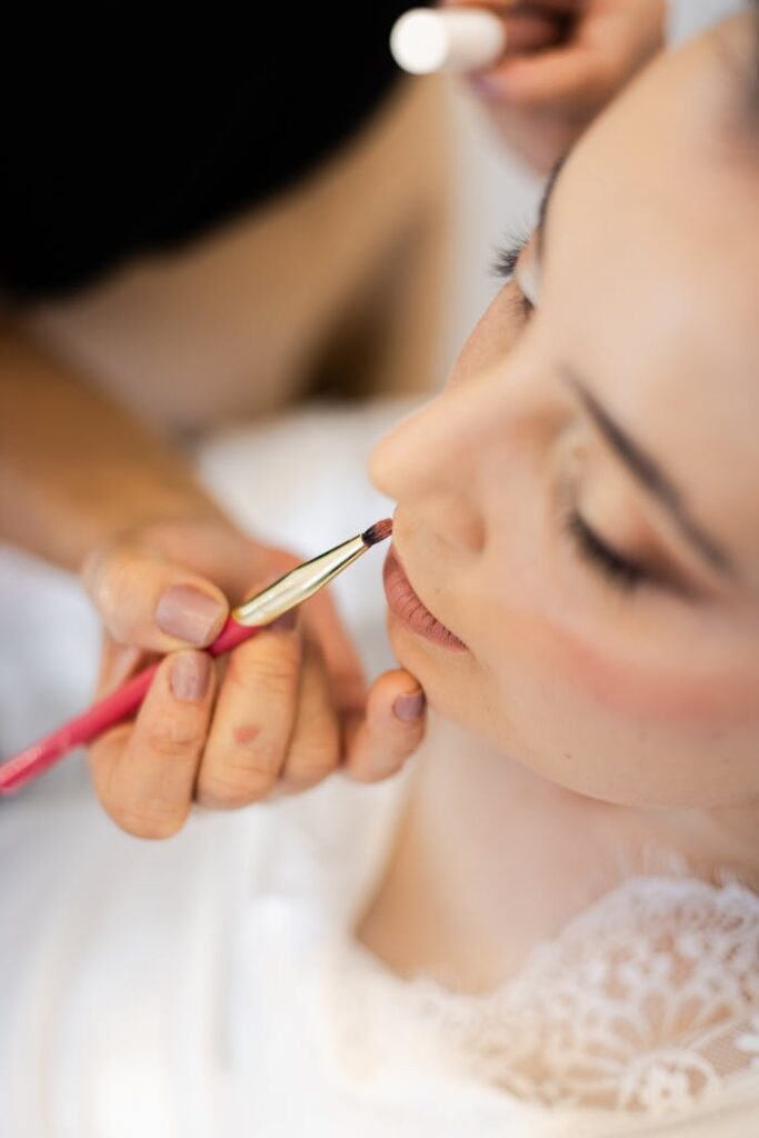 Primer plano de la piel de una novia siendo preparada con una brocha profesional para asegurar un maquillaje de novia duradero y luminoso.